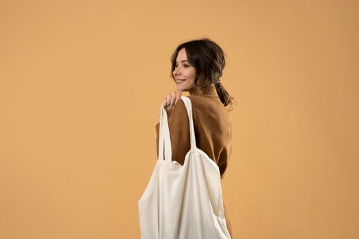 Young woman holding reusable mesh bag with groceries over orange background. Zero waste, plastic free concept. Eco lifestyle. Eco shopping. Conscious consumption. Eco trend