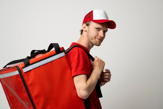 Side view delivery employee man 20s in red cap t-shirt uniform thermal food bag backpack work courier service