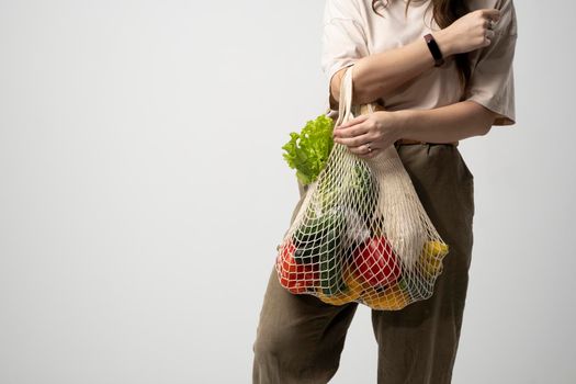 Happy woman holding reusable cotton shopping bag with groceries, bread and greens. Concept of no plastic. Zero waste, plastic free. Sustainable lifestyle