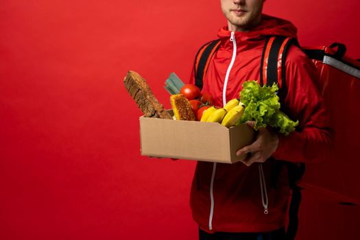 Smiling delivery man in a red uniform and a cap with a thermal bag giving grocery bag to customer at home. Online food shopping service concept