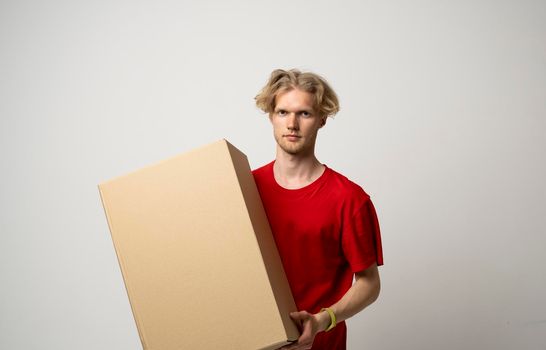 Male employee in in red uniform working as courier dealer and holds cardboard box isolated on white background, studio portrait. Service concept. Mock up copy space