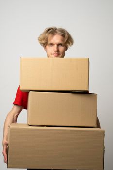 Cheerful delivery man. Happy young courier holding a cardboard boxes and smiling while standing against white background. Delivery man holding pile of cardboard boxes in front of himself