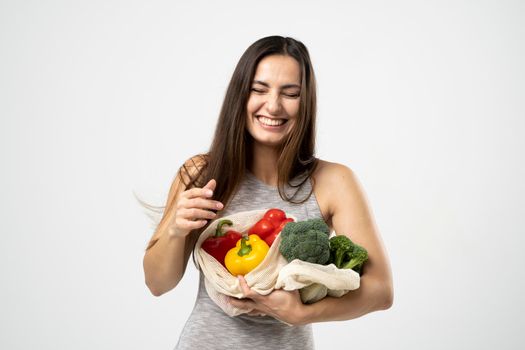 Smiling brunette girl is holding mesh shopping bag with vegetables, greens without plastic bags. Zero waste, plastic free Eco friendly concept. Sustainable lifestyle