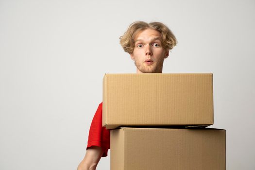 Cheerful delivery man. Happy young courier holding a cardboard boxes and smiling while standing against white background. Delivery man holding pile of cardboard boxes in front of himself