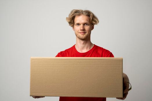 Portrait of smiling male in red t-shirt carrying delivery package on white background