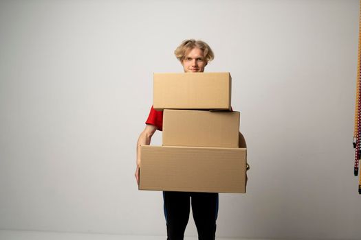 Cheerful delivery man. Happy young courier holding a cardboard boxes and smiling while standing against white background. Delivery man holding pile of cardboard boxes in front of himself