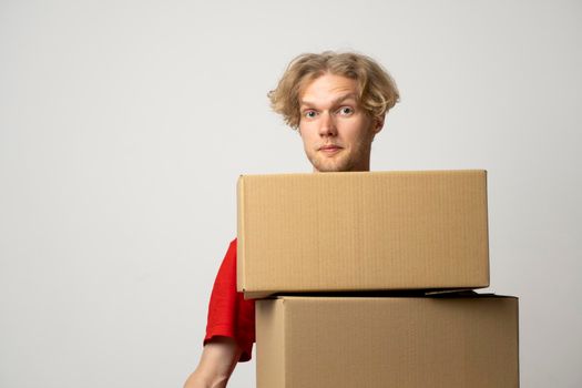 Delivery man employee in red cap and t-shirt uniform holds a stack of cardboard boxes, parcels isolated on white background studio