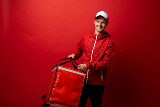 Young delivery man with thermal backpack opening a bag for give a products to a client. Fast food delivery service