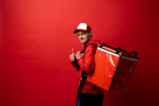 Delivery boy with red thermal bag showing a thumb up. Fast and convenient food delivery service for self-isolated citizens during an epidemic of viral disease. Boy delivering food to customers