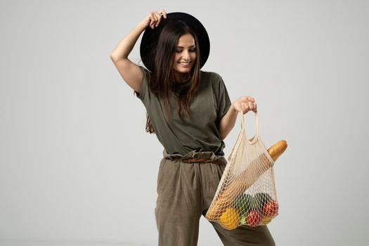 A modern stylish woman with a mesh shopping bag with vegetables against the background of the studio. The concept of healthy nutrition, vegetarianism and ecology. Refusal of plastic bags