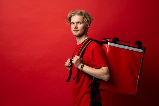 Portrait of happy smiling delivery man in a red t-shirt with thermal insulated bag on a shoulder looking in a camera. Food delivery service