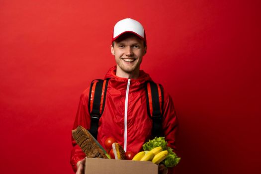 Delivery man in a red uniform with a thermal bag on a shoulder delivering food to a customer at home. Online grocery shopping service concept