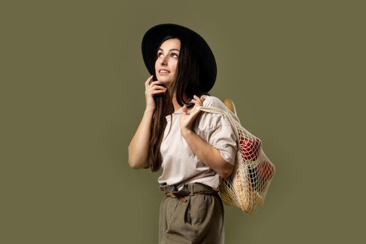 Woman in a beige t-shirt and a hat holding mesh shopping bag with groceries. Conscious consumption. Eco trend. Zero waste concept. Girl carry bag shopper