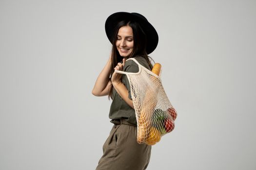 Zero waste concept. A young girl holds on her shoulder a textile mesh eco bag with a groceries. The girl smiles, wearing a beige t-shirt and hat. Refusal of plastic bags