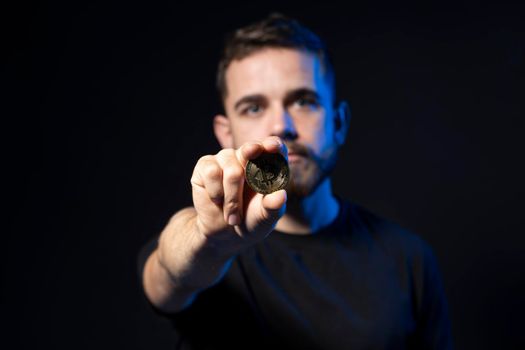 A young bearded man is holding excited a bitcoin looking at the camera. BTC the new virtual money