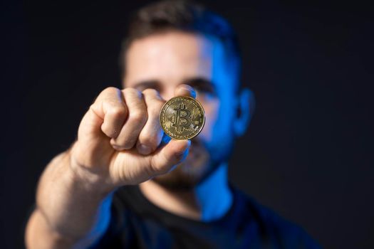 Young bearded man holding virtual currency bitcoin coin. Crypto trader holding a btc coin. Cryptocurrency