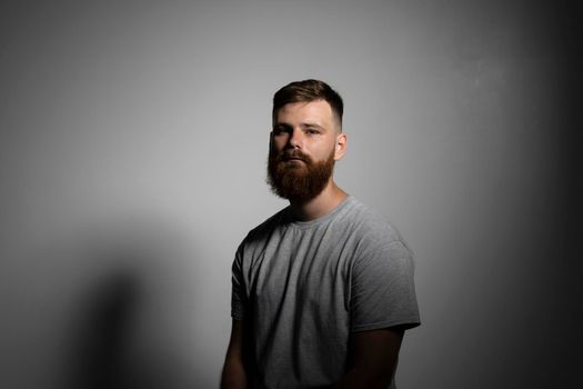 Close-up portrait of a handsome a brunette brutal bearded man in a grey t-shirt. Stylish and handsome man with a beard