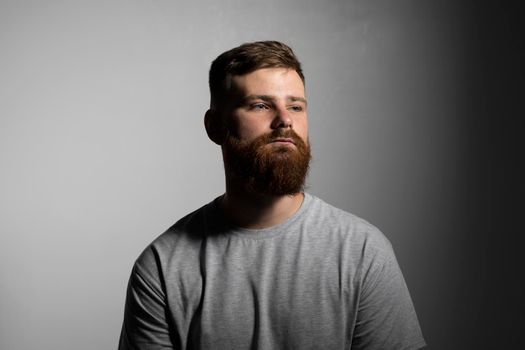 Close-up portrait of a handsome a brunette brutal bearded man in a grey t-shirt. Stylish and handsome man with a beard