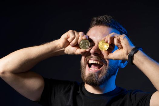 Happy bitcoin lover with golden coin by eyes. Digitall symbol of a new virtual currency. Cryptocurency