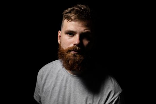 Portrait of handsome serious unshaven guy with long beard and handlebar moustache in grey t-shirt looking forward