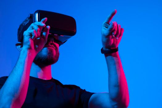 Young bearded man in virtual reality helmet plays online game in metaverse. Game simulates behavior in fictional world, gadgets and virtual reality addiction. Future technology concept