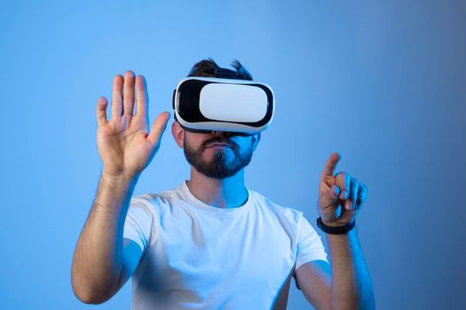 Bearded man with glasses of virtual reality in a neon light. Future technology concept. Young man touching air while wearing VR glasses