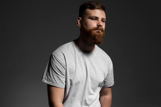 Close-up portrait of a handsome a brunette brutal bearded man in a grey t-shirt. Stylish and handsome man with a beard