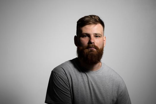 Close-up portrait of a handsome a brunette brutal bearded man in a grey t-shirt. Stylish and handsome man with a beard