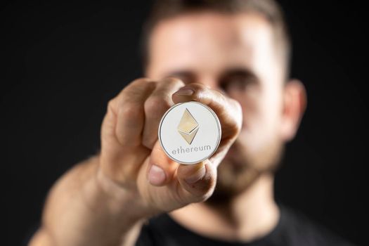 Young bearded man holding virtual currency ethereum coin and bitcoin. Cryptocurrency