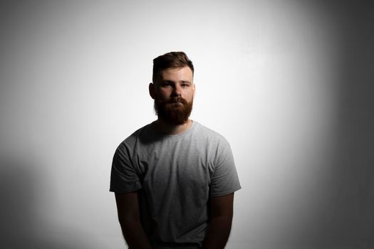 Close-up portrait of a handsome a brunette brutal bearded man in a grey t-shirt. Stylish and handsome man with a beard