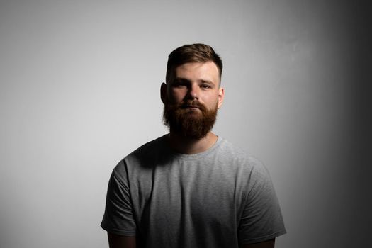 Close-up portrait of a handsome a brunette brutal bearded man in a grey t-shirt. Stylish and handsome man with a beard