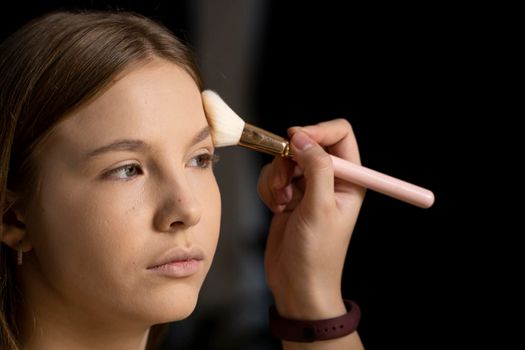 Close up face of beautiful young woman getting powder on her cheek with a brush. Professional makeup artist