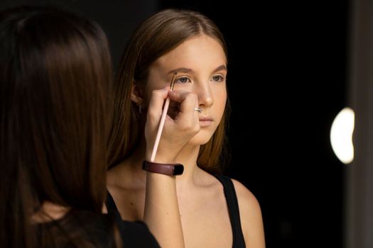 Makeup artist doing a eyebrows makeup on a beautiful woman face. Hand of make-up master is painting eyebrow of young beauty model girl. Make up in process