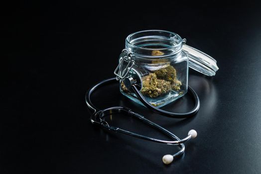 the Dry medical cannabis in a jar with a stethoscope on a black background