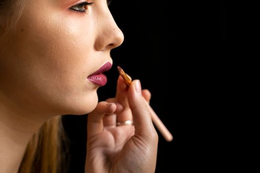 Makeup artist applies red lipstick on a beautiful woman face. Hand of make-up master, painting lips of young beauty model girl. Make up in process