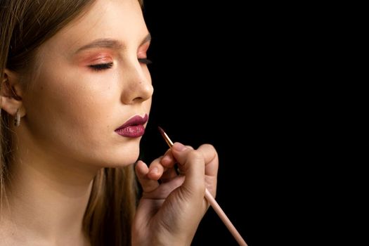 Makeup artist applies red lipstick on a beautiful woman face. Hand of make-up master, painting lips of young beauty model girl. Make up in process