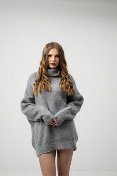 Beautiful young woman portrait in a long sweater. Studio shot, isolated on gray background