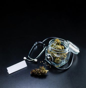 the Dry medical cannabis in a jar with a stethoscope on a black background