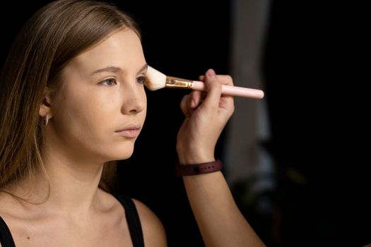 Makeup artist applying liquid tonal foundation on the face of the woman in make up room. Professional make-up artist working with brush on model face