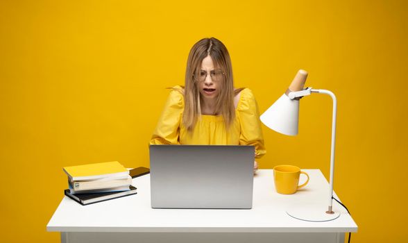 Young indignant confused secretary employee business woman with a spread hands in yellow shirt sit work at white office desk use pc laptop computer