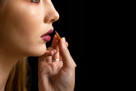 Makeup artist applies red lipstick on a beautiful woman face. Hand of make-up master, painting lips of young beauty model girl. Make up in process