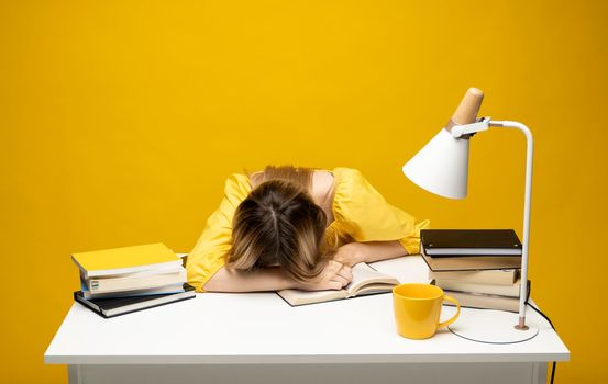 Student studying exam and sleeping on books on a yellow background. Tired student girl with glasses sleeping on the books in the library