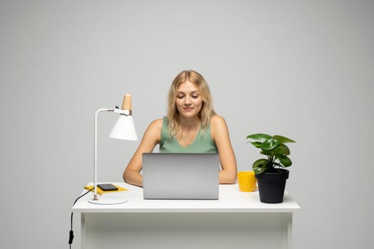 Portrait of a pretty young woman studying while sitting at the table with grey laptop computer, notebook. Smiling business woman working with a laptop isolated on a grey background