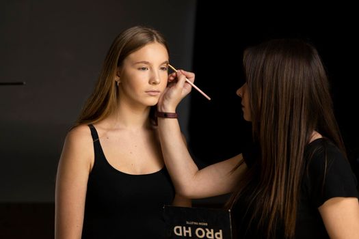 Makeup artist doing a eyebrows makeup on a beautiful woman face. Hand of make-up master is painting eyebrow of young beauty model girl. Make up in process