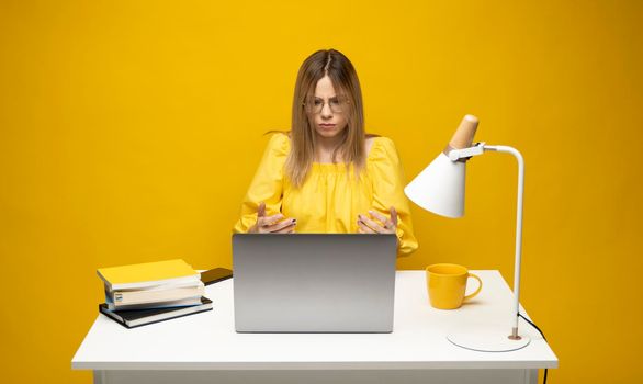 Young indignant confused secretary employee business woman with a spread hands in yellow shirt sit work at white office desk use pc laptop computer