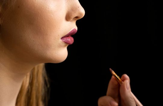 Makeup artist applies red lipstick on a beautiful woman face. Hand of make-up master, painting lips of young beauty model girl. Make up in process