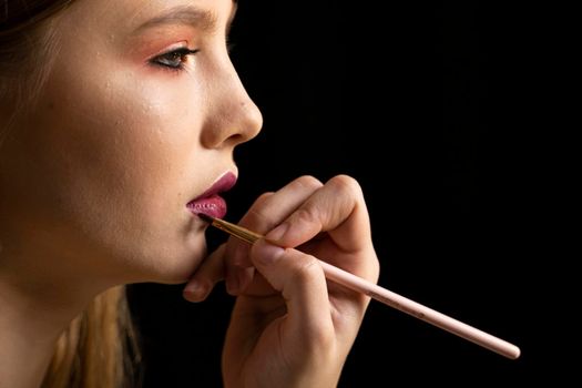 Close up of hand of visagiste applying lipstick on female lips