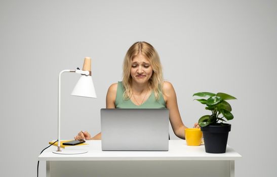 Confused beautiful young blonde business woman or student at the desk with a laptop. Business and education concept