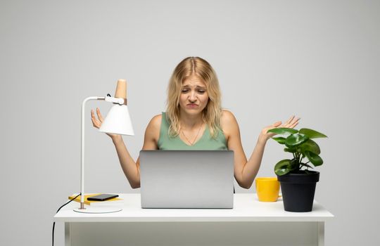 Confused designer woman in a green t-shirt looking at her laptop in a bright creative office. Business and education concept