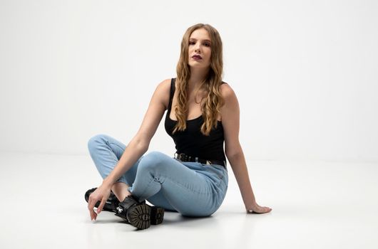 Beautiful young woman portrait in a black t-shirt and blue jeans. Studio shot, isolated on gray background